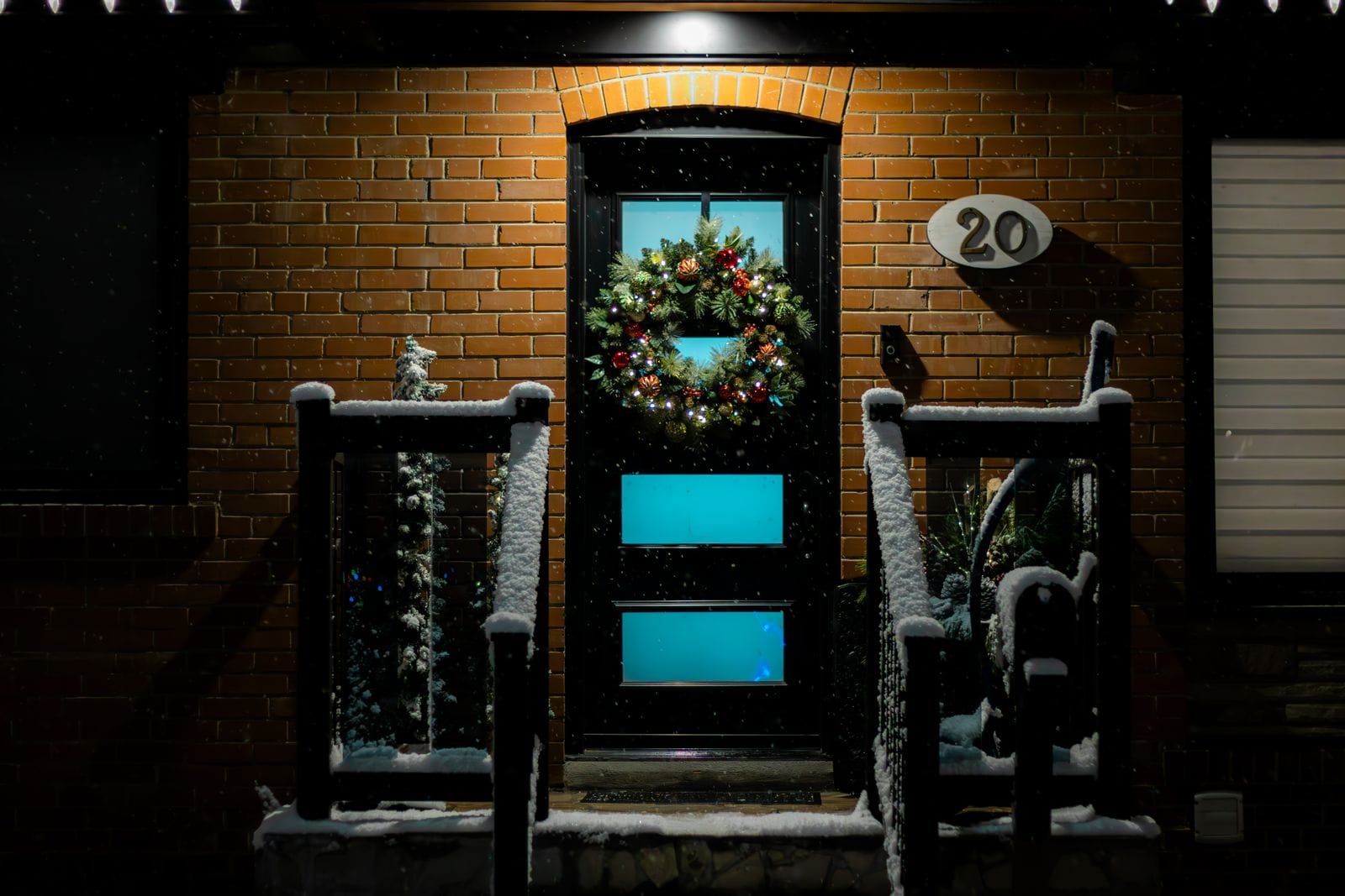 Front door decorated with a lit wreath and garland